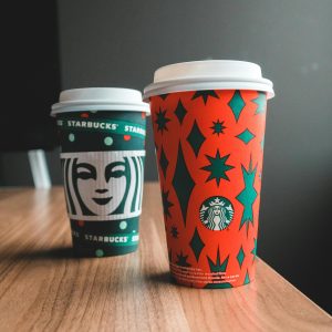 Close-up of Starbucks holiday-themed cups on a wooden table indoors.